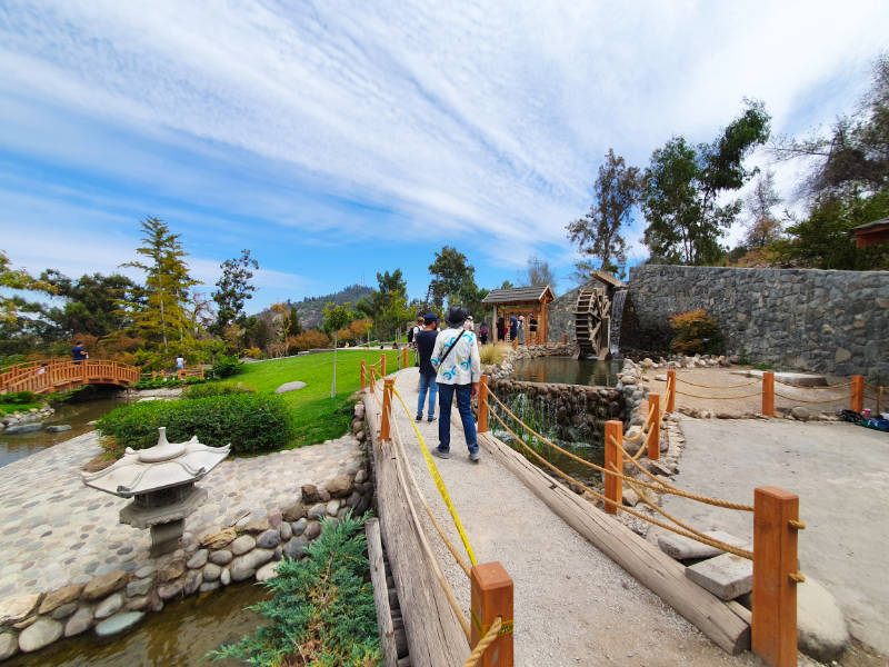 Personas cruzando el Puente de Piedra del Jardín de la Amistad Japonesa Chilena en el Cerro San Cristóbal - Se ve un farol de piedra y el molino de agua - Foto de Andrea Hoare Madrid