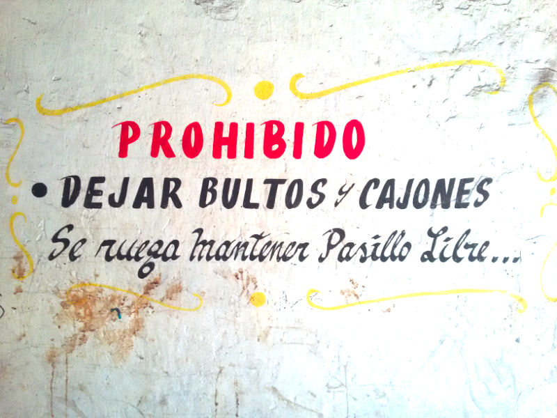 Aviso antiguo pintado en una muralla del Mercado Estación Central con caligrafía antigua, dice: "Prohibido dejar bultos y cajones. Se ruega mantener el pasillo libre". Foto de Andrea Hoare Madrid